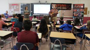 A man plays a guitar at the front of a classroom