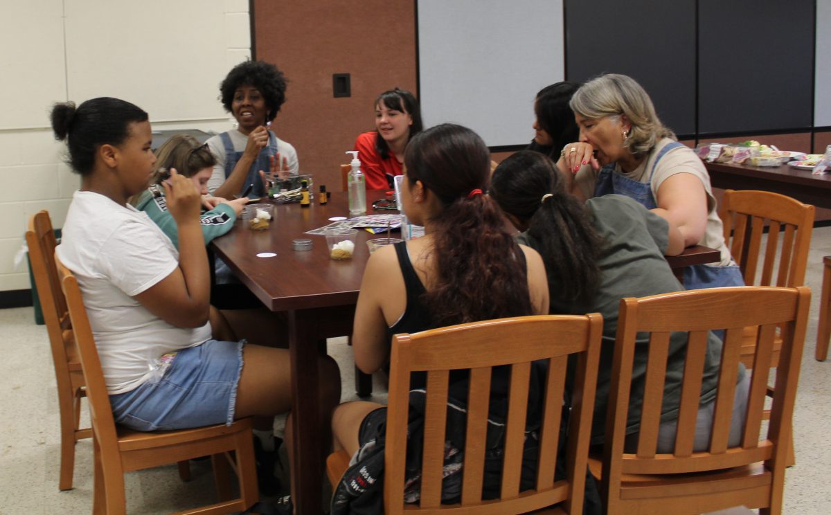 A girl samples a fragrance as other students and two adults sit around a table.