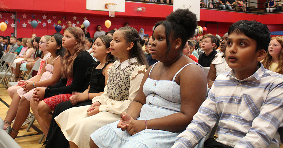 Students sit in chairs watching a speaker on stage.