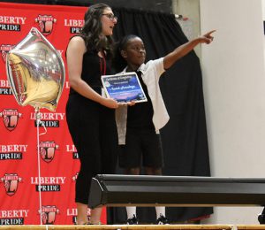 A student points to where family is in the crowd as a teacher presents a certificate