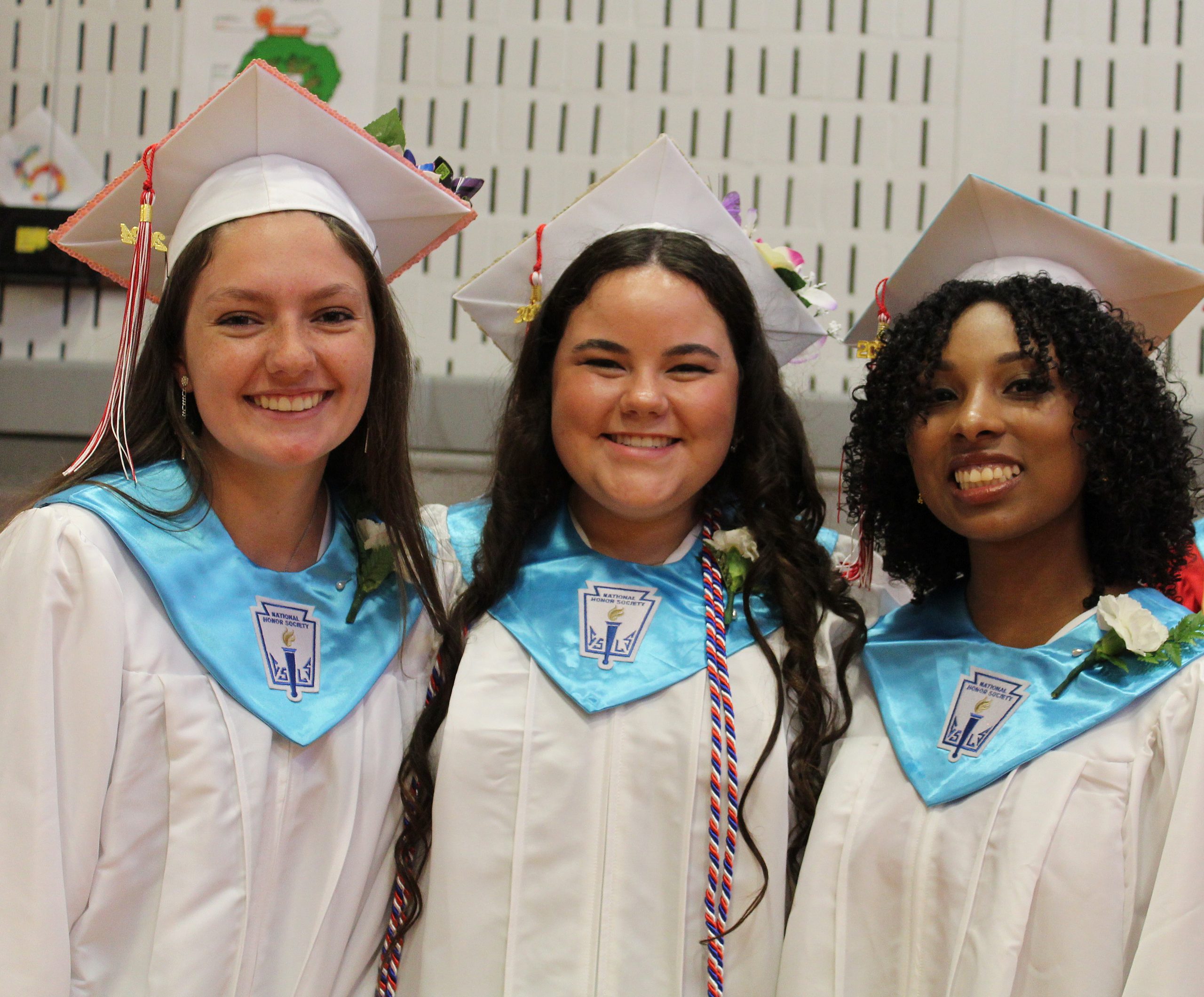 IMG_7428 Three students in caps and gowns and honor society stoles pose for a photo.