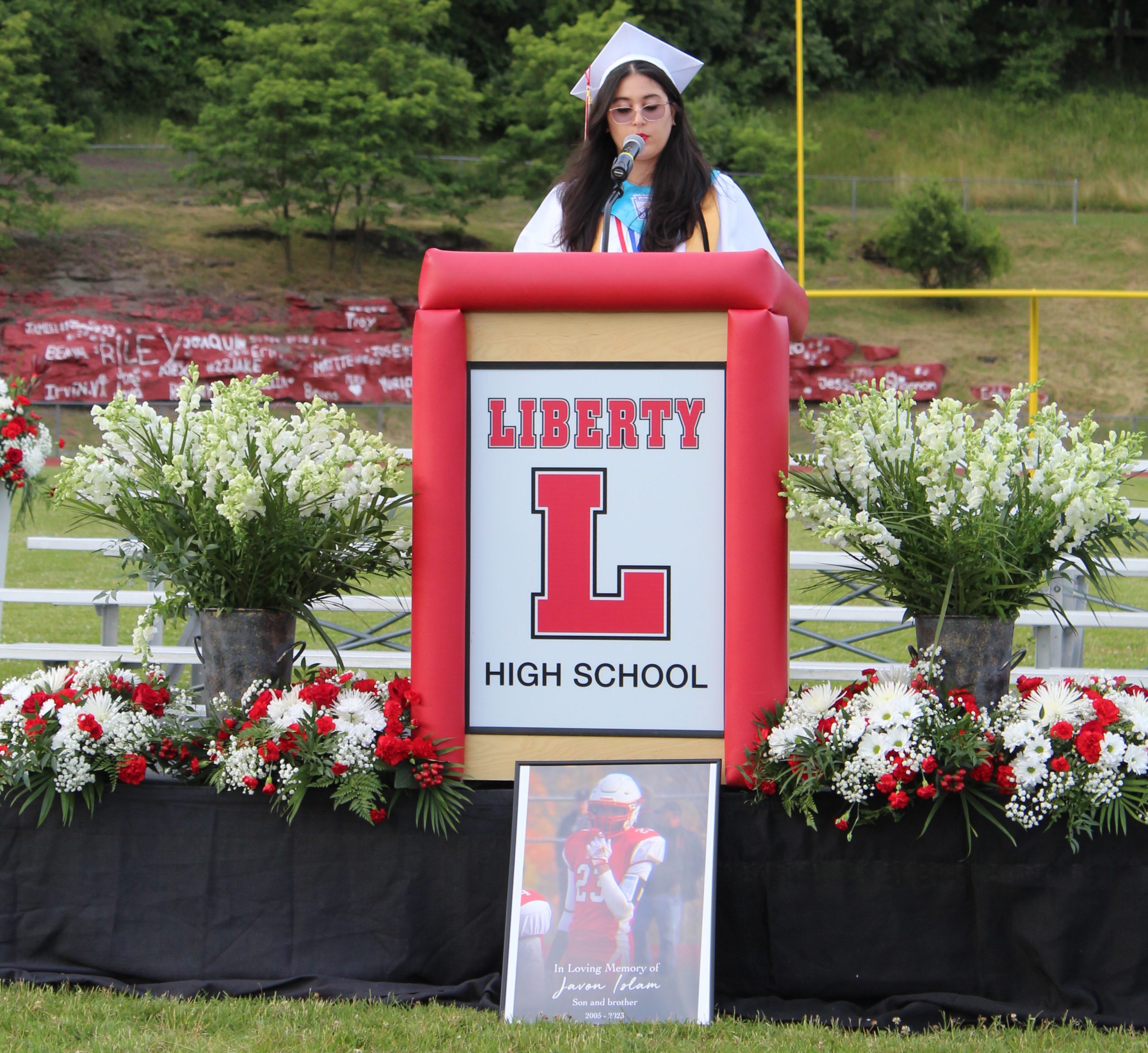 IMG_7545 A graduate speaks at a podium with a framed photo of a classmate sitting below the podium.