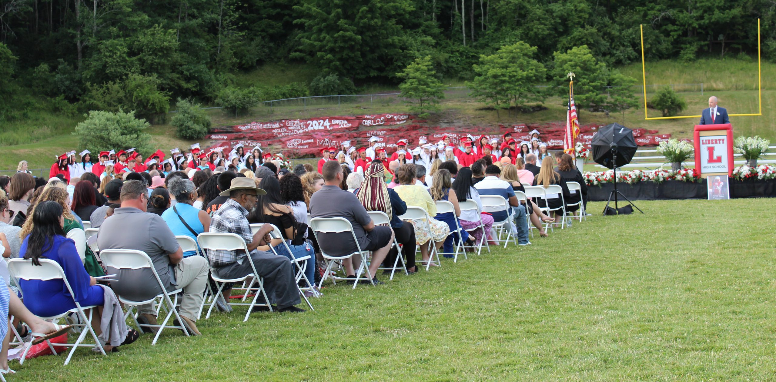 IMG_7576 A man speaks at a podium with the graduates behind him as the audience watches