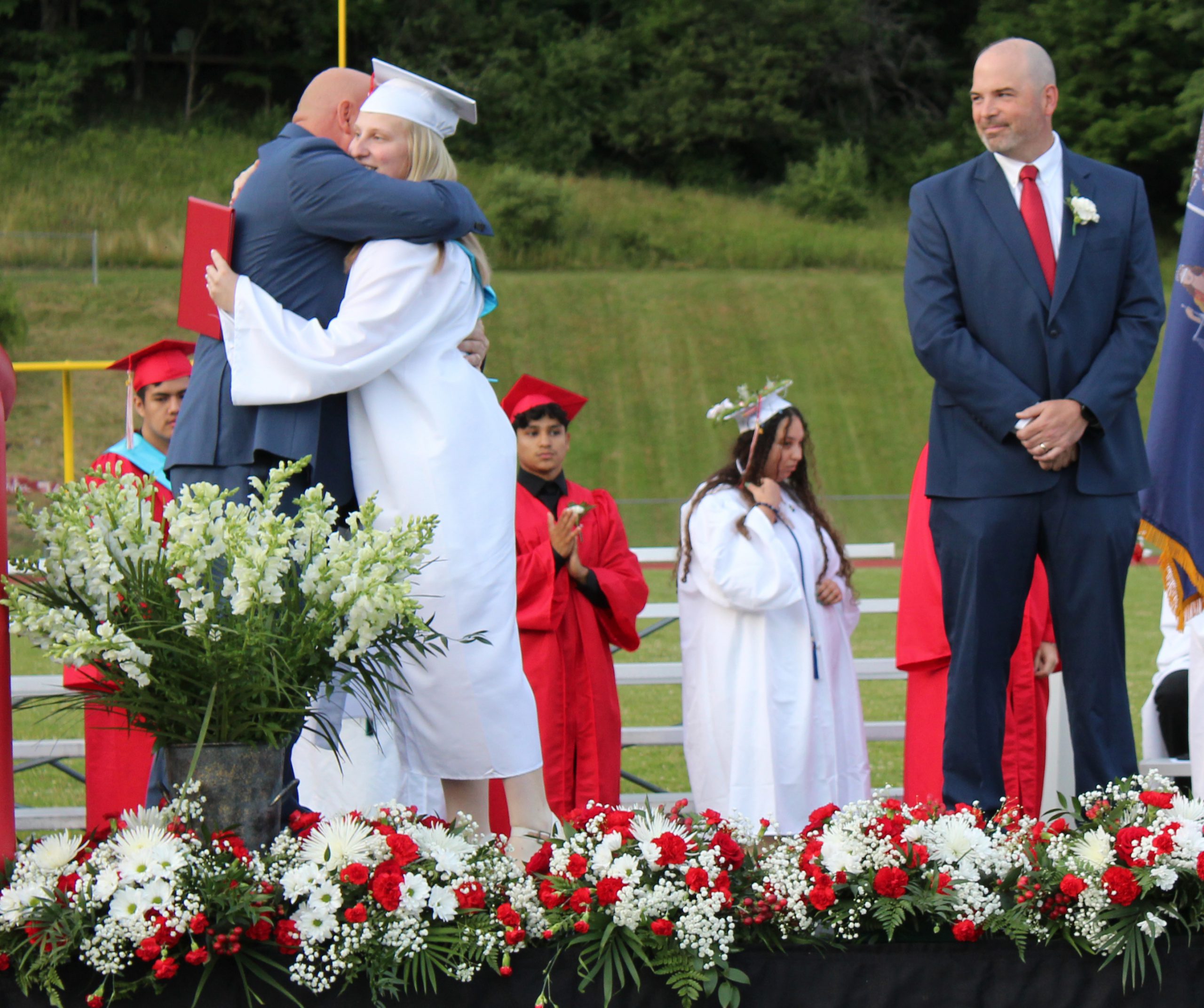 IMG_7616 A graduate hugs an adult after she receives her diploma as a man watches