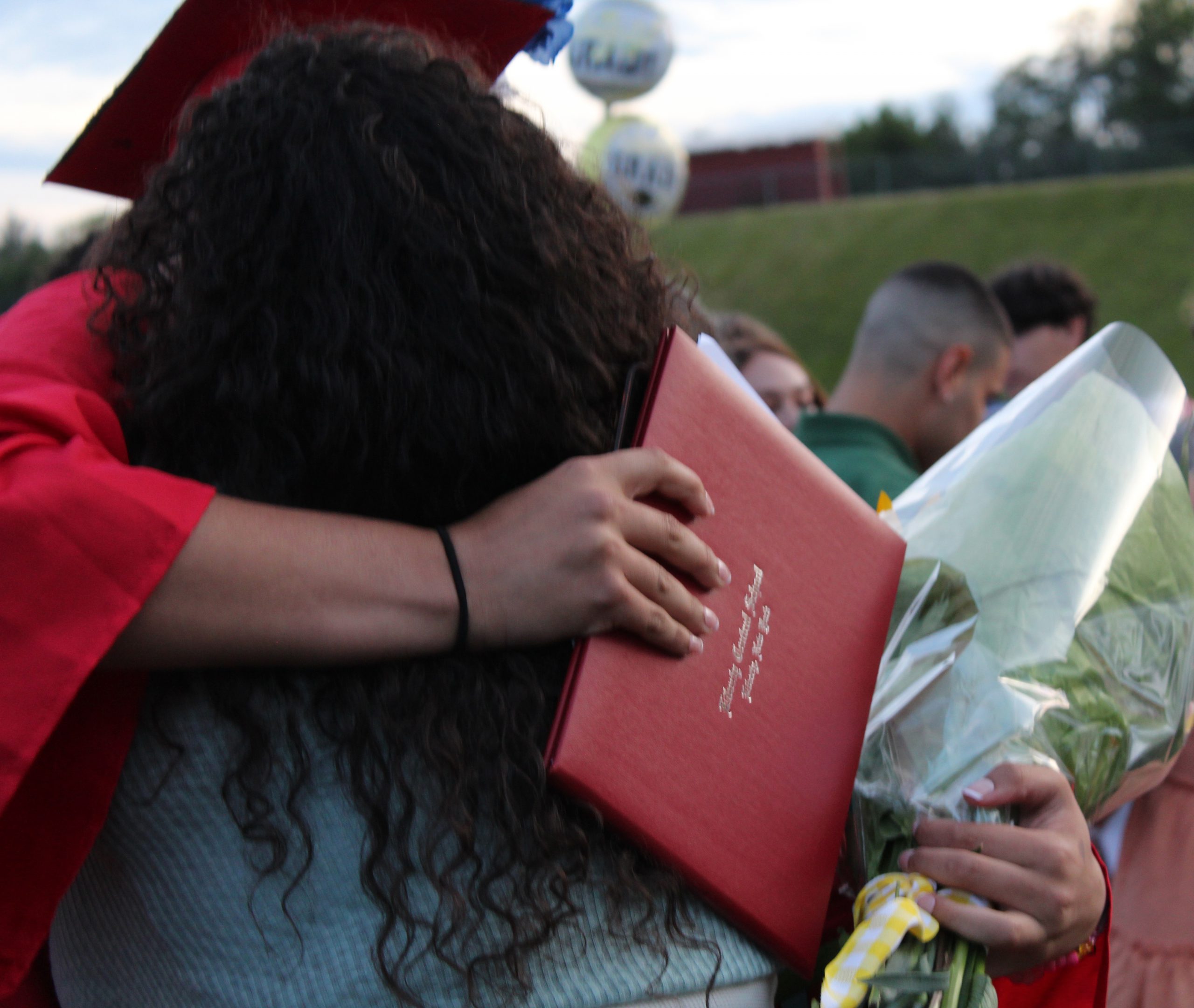 IMG_7726 A graduate holding a diploma and flowers hugs an adult