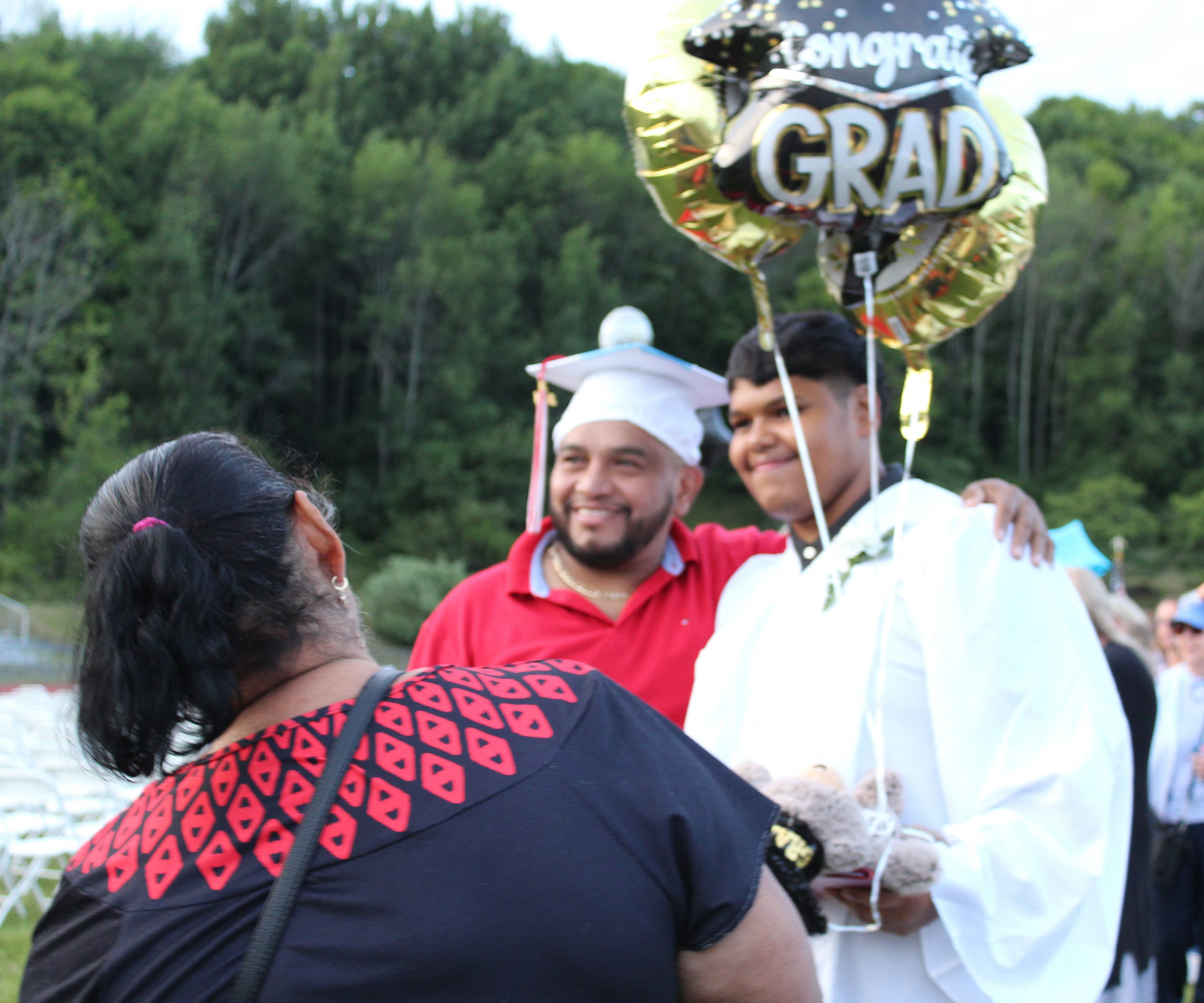 IMG_7734 A woman watches as a man poses with a student in a gown holding balloons as the man wears the cap