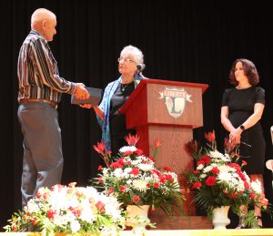 A woman hands a man a box standing while standing behind a podium as a woman watches.