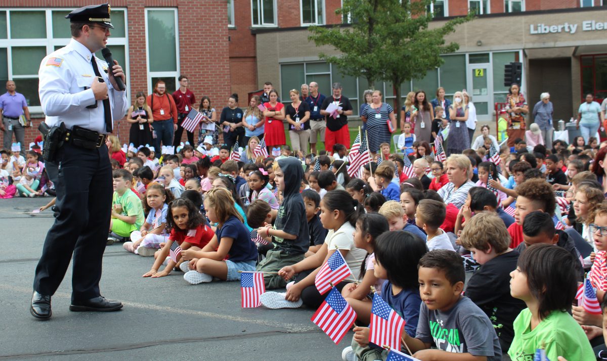 A man speaks in front of a crowd of students holding american flags