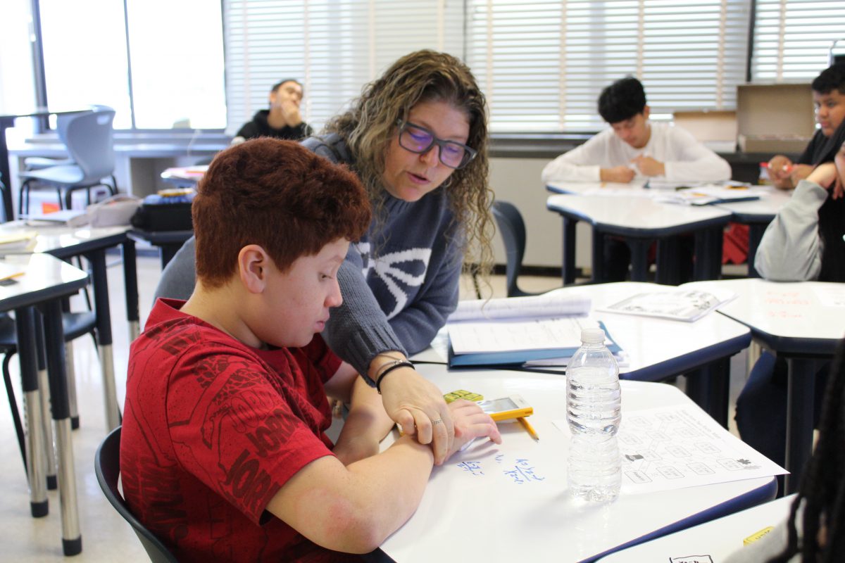 A teacher looks over a students work that was written on an erasable desk.