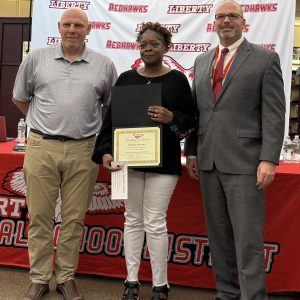 A woman holds a certificate and a a piece of paper with a pin on it flanked by two men.