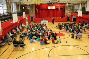 A magician performs in front of students seated on a gym floor