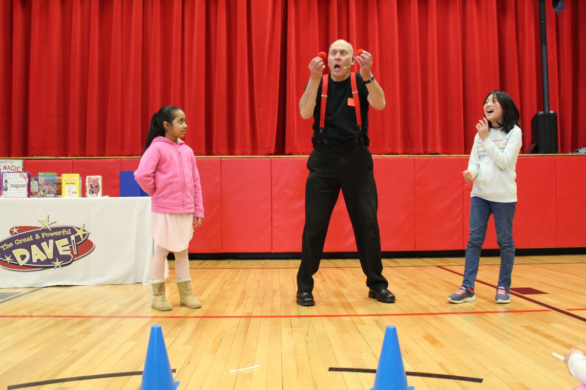A man holds two squishy bulbs as a student at left laughs and another student watches