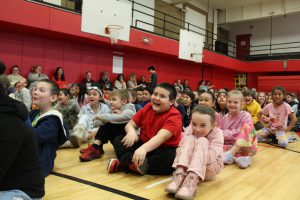 Students sitting on a gym floor laugh