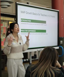A person talks in front of a large screen on MAP Growth Basics for Teachers