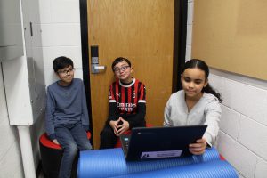 Three students watch a video on a laptop while seated in a nook.