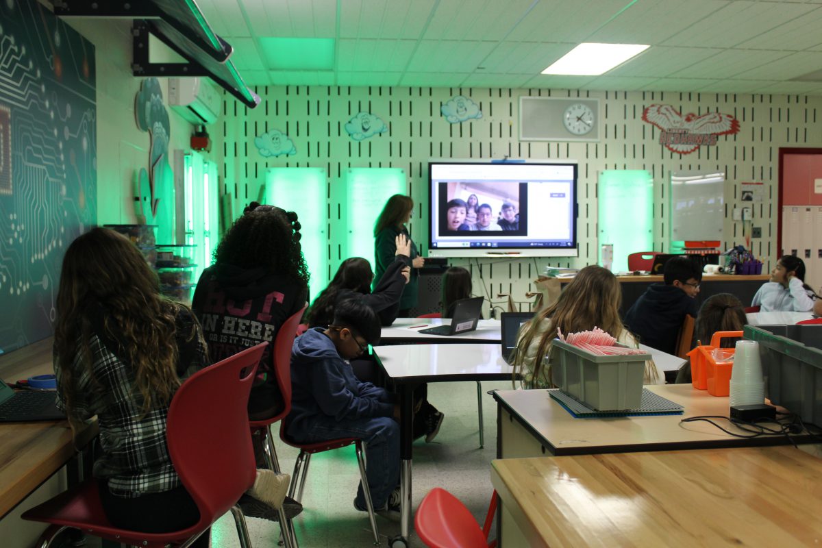 Students and a teacher watch a video on the big screen