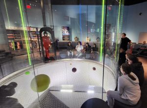 Students watch as a variety of balls and other objects move in a vertical wind tunnel