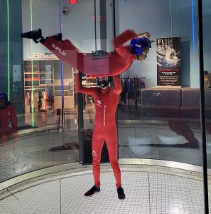 A student flies and is supported by an instructor in the wind tunnel
