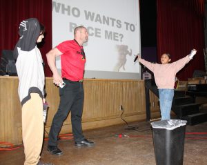 A student spreads her arms as a man speaks and another student watches