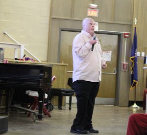 A man who was disfigured in an IED attack in Iraq speaks in an auditorium