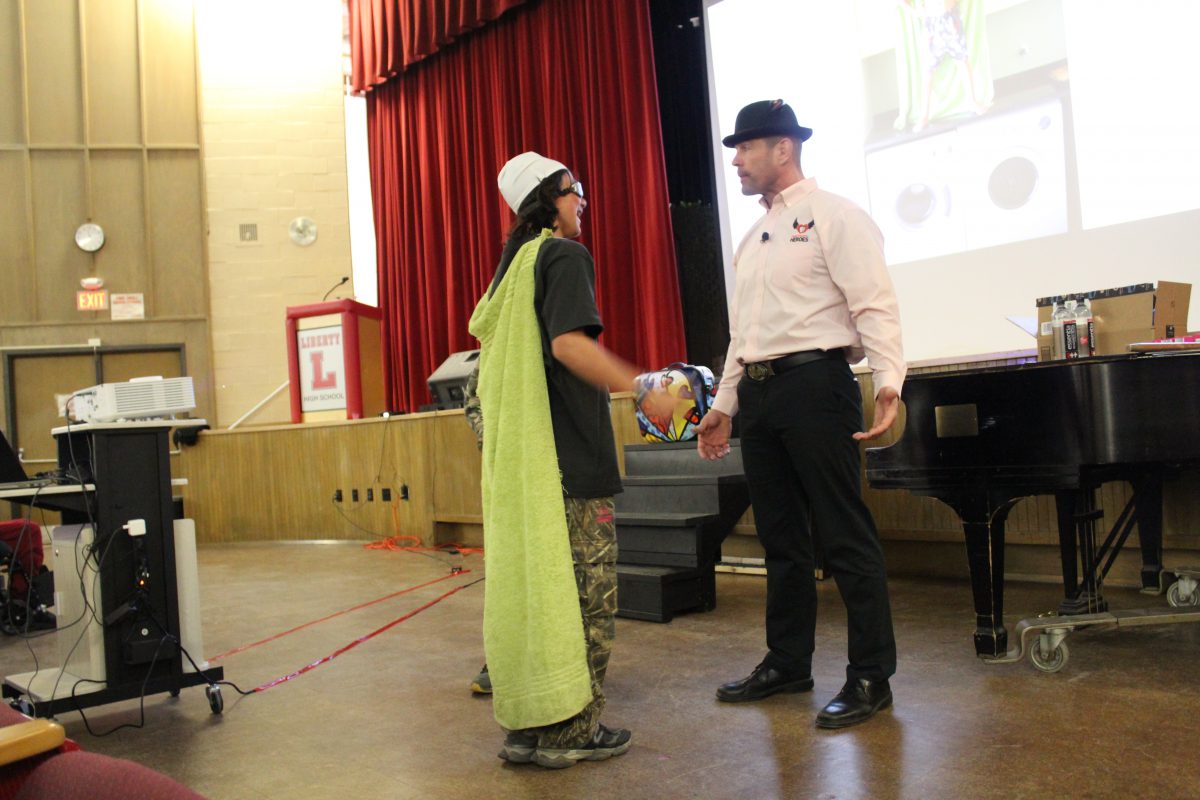 A student wearing a towel as a cape confronts a man playing a bully.