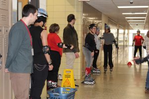 Students gather around a teacher, all on rollerblades in a hallway
