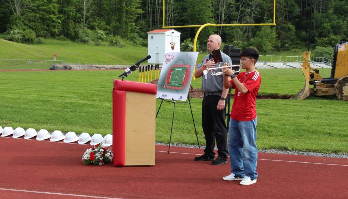 groundbreaking2 A student plays the trumpet as a man stand behind a podium with his hand on his heart