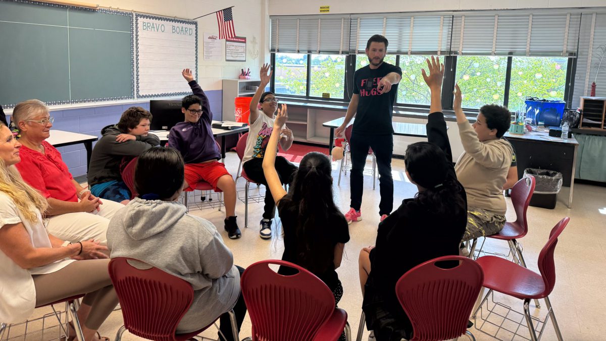 A man points at students raising their hands while seated in a circle.
