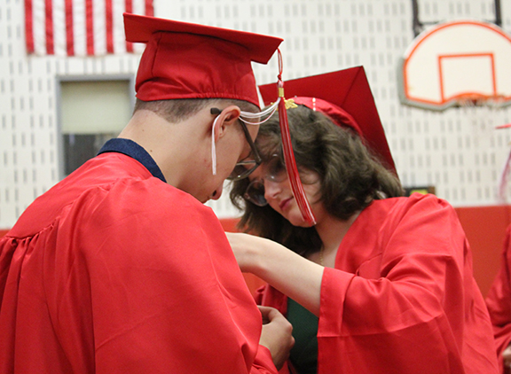 graduation25 A graduate helps another graduate put a flower on his robe.