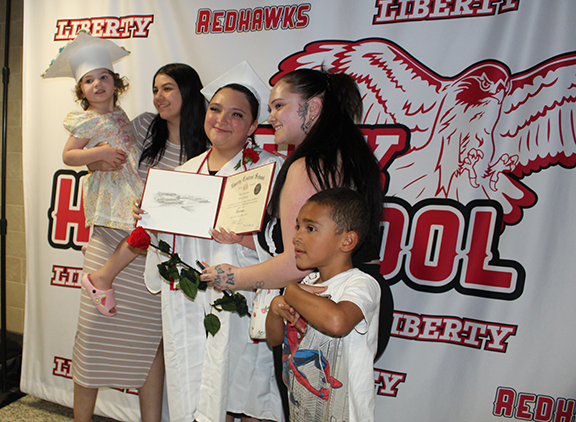 graduation 2 A family poses for a photo with a young girl wearing a graduation cap in front of a LHS background