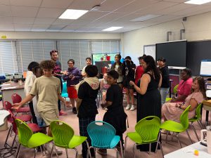 Students and adults stand up from colorful chairs placed in a circle