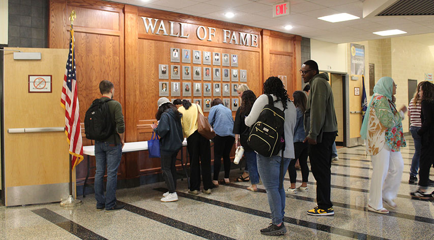 Faculty and staff sign in at a table in front of the wall of fame.