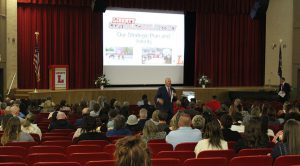 A man in front of a screen with "Our Strategic Plan and intents" on a screen.