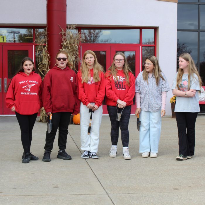 students stand in front of the school holding tools for planting