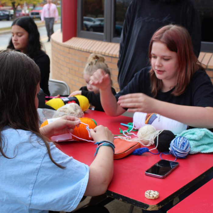 A student shows another student how to crochet