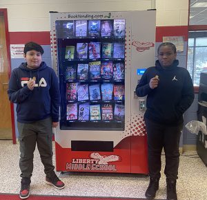 Two students hold coins the earned to use in the book vending machine.
