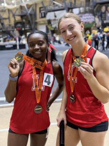 Two Liberty athletes hold up their medals at an indoor track and field meet.