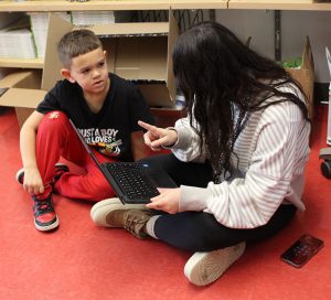 A teacher talks to a student seated on a floor