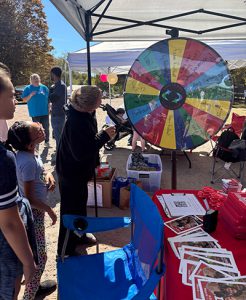 A person spins a colorful wheel under a tent near a table covered with Liberty brochures