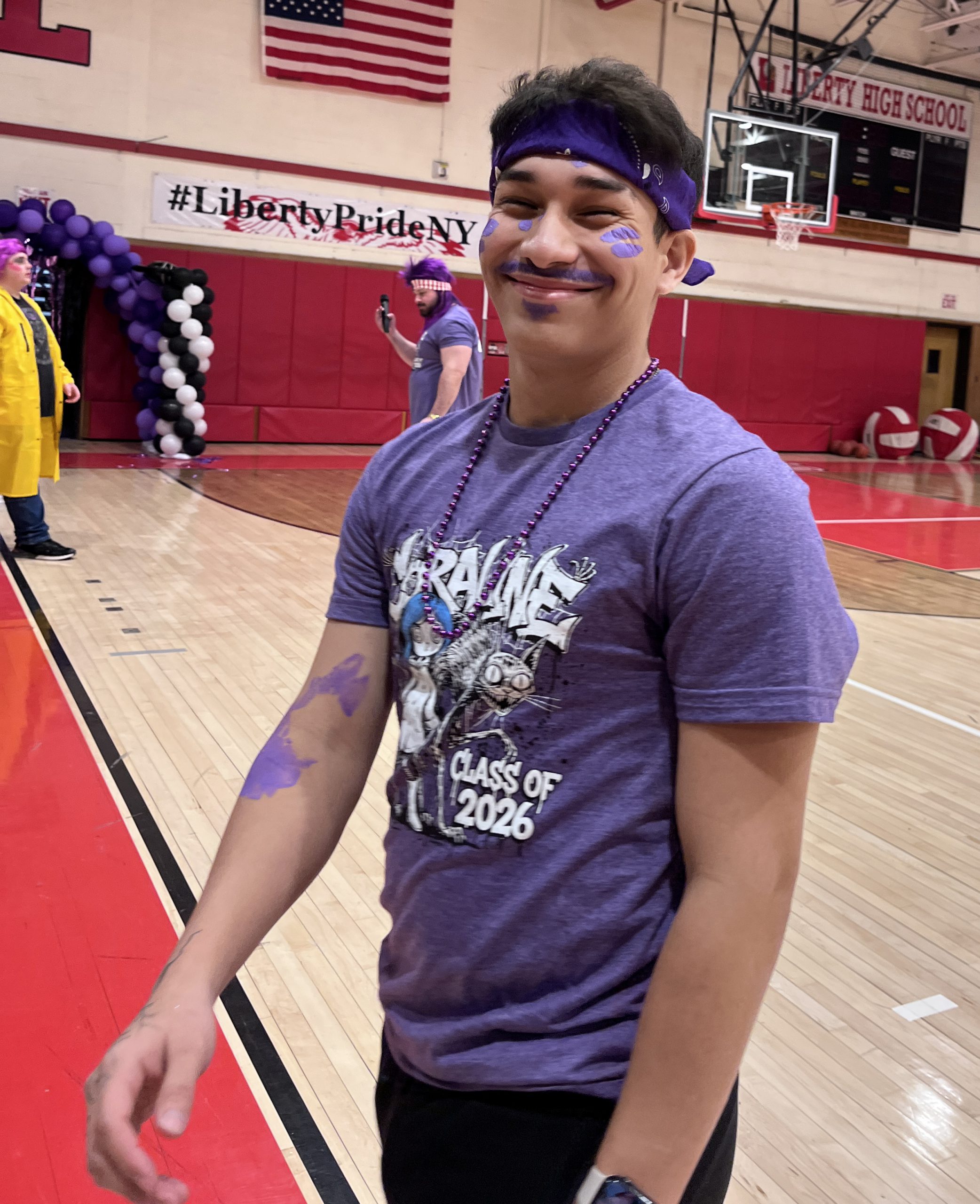 A student is dressed in a Class of 2026 "Coraline" shirt with purple spots on his face