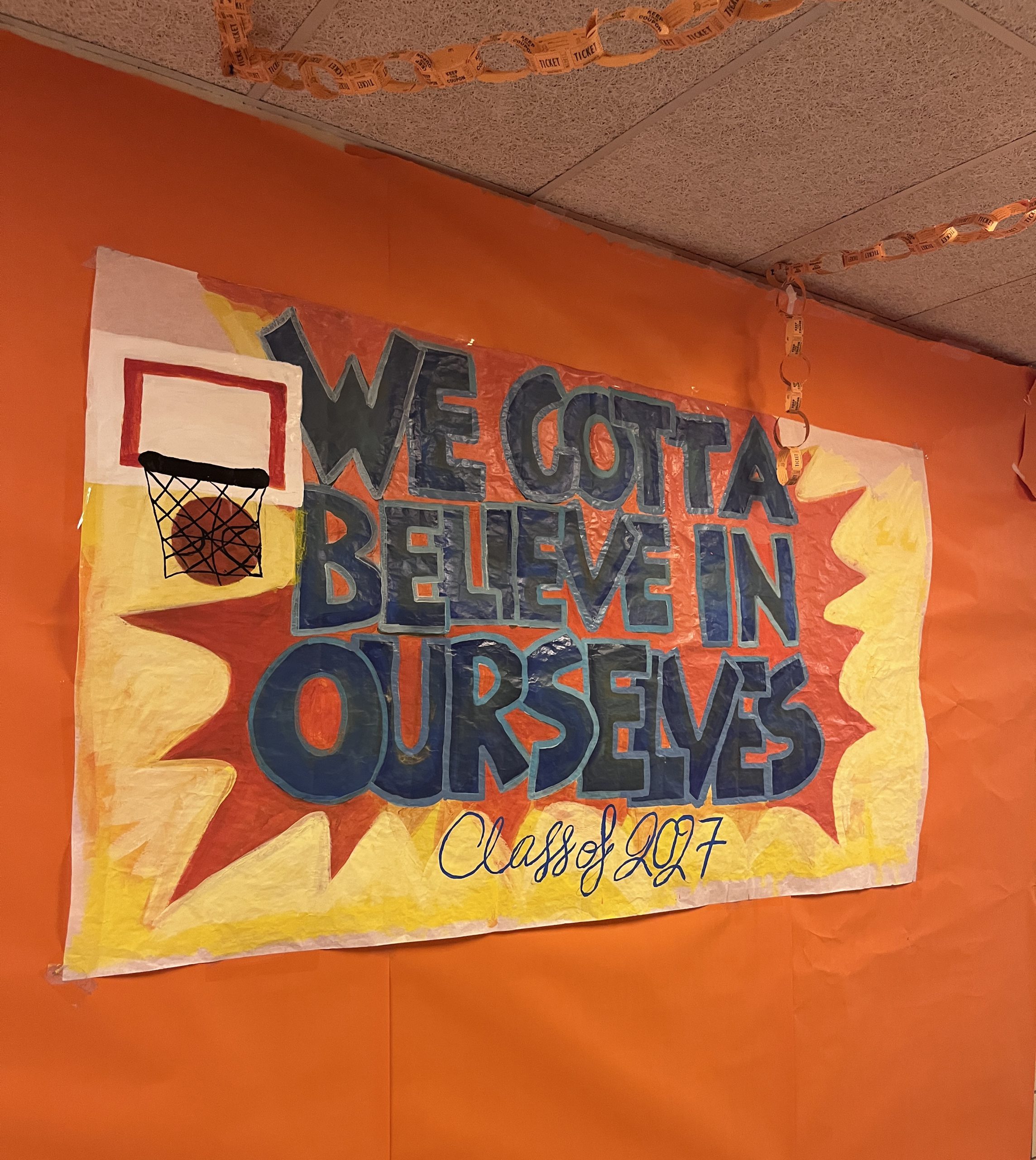A sign reads we gotta believe in ourselves Class of 2027 in a Space Jam orange theme.