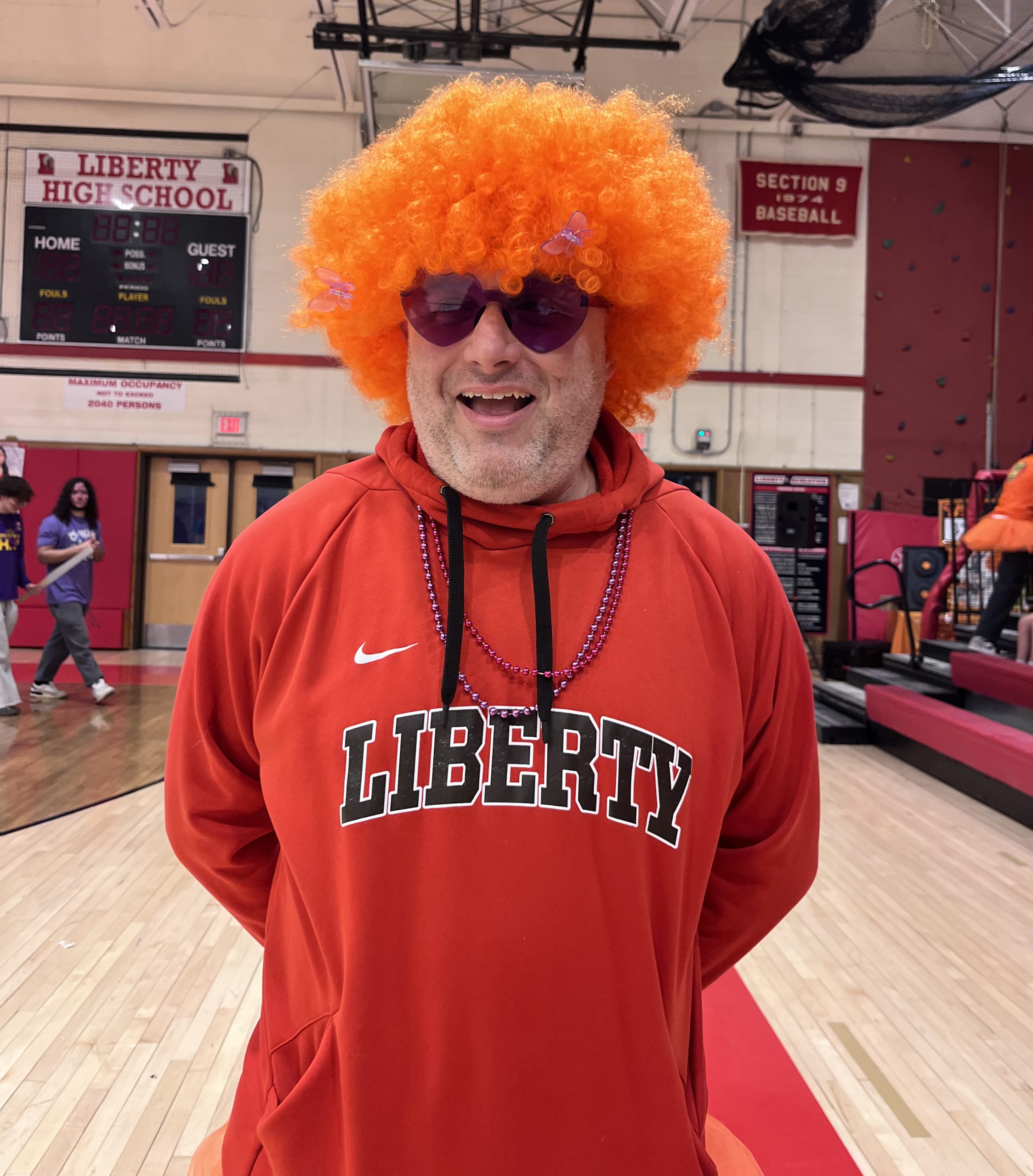 A staff member wears an orange wig and Liberty sweatshirt