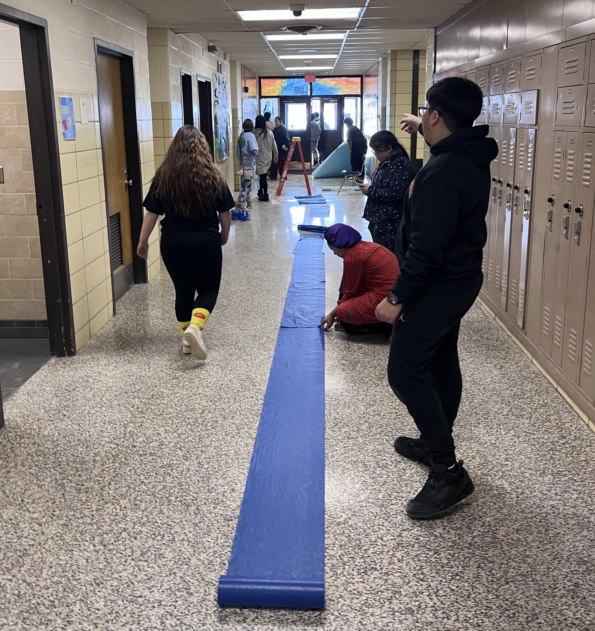 Students roll out blue vinyl cloth in a hallway