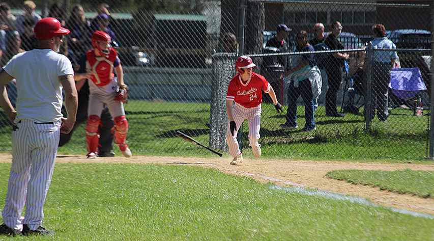 A batter drops his bat and runs for first base at the first base coach and catcher watch