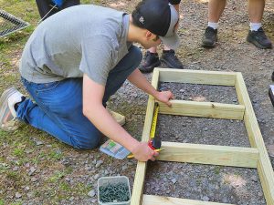 A student measures the space between two pieces of wood for the seat of a bench.
