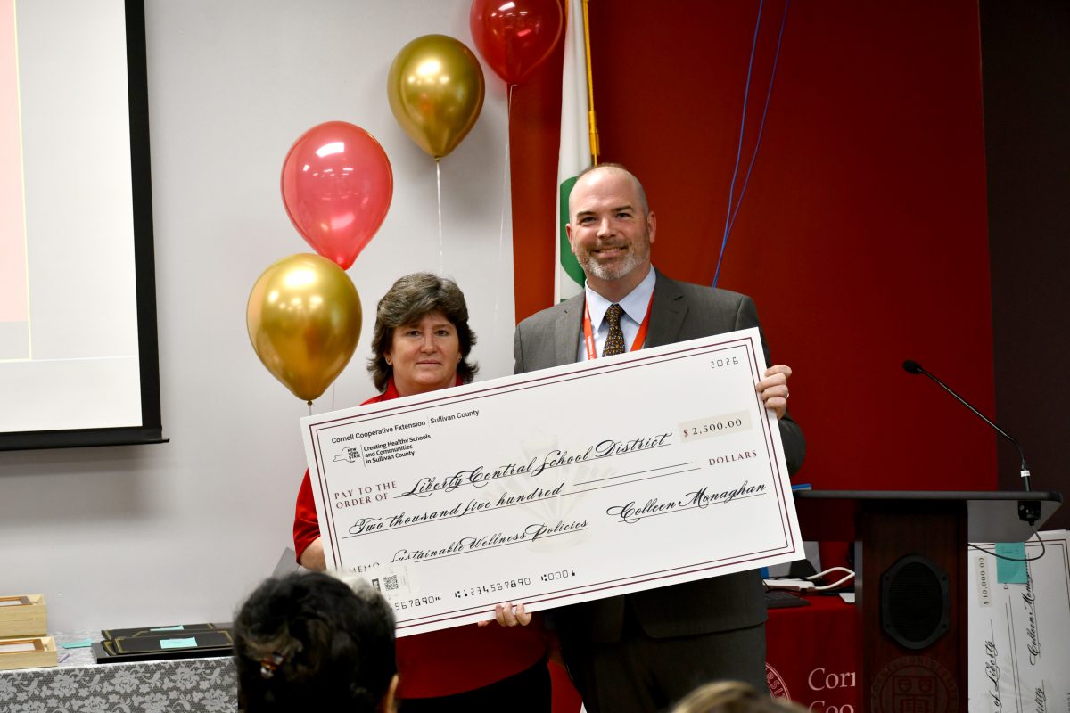 Two people pose holding a large check