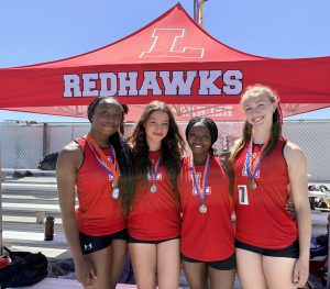Four students pose with medals in front of a redhawks tent/