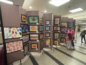 People look at artwork hung on a portable accordion wall