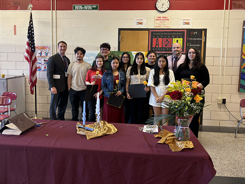 Students and adults pose for a photo in front of a table set up for an induction ceremony